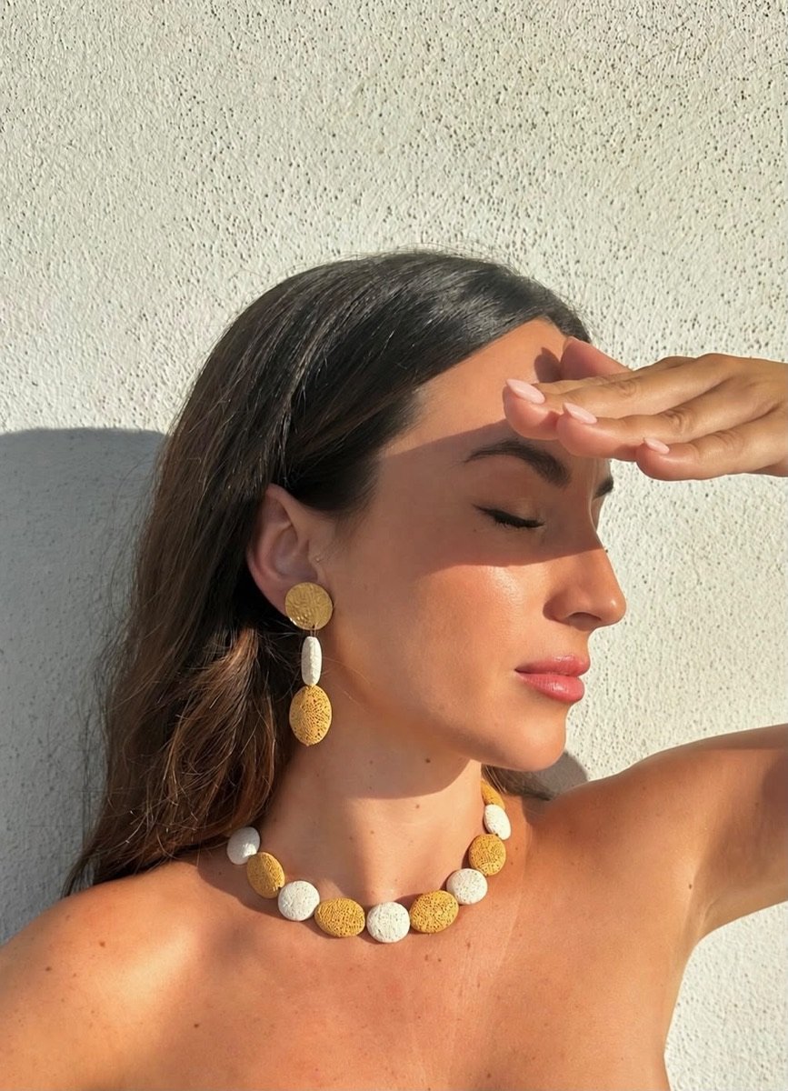 Mujer protegiéndose del sol con los pendientes y el collar CALIA blanco y ocre