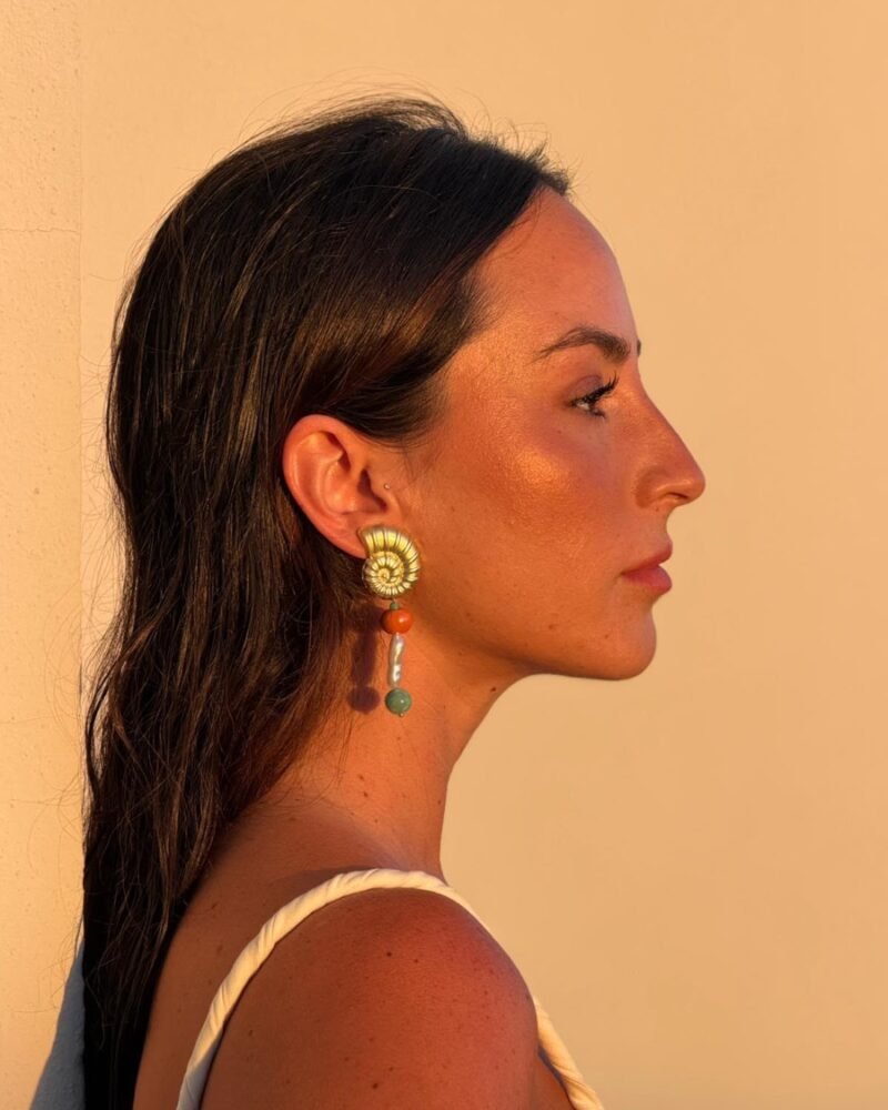 Mujer de perfil luciendo el pendiente Marea naranja con caracola dorada