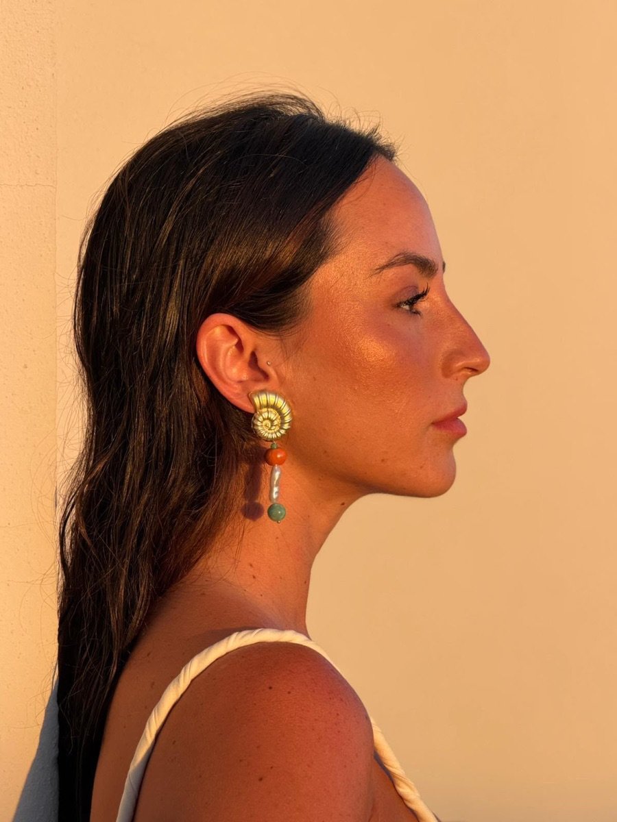 Mujer de perfil luciendo el pendiente Marea naranja con caracola dorada